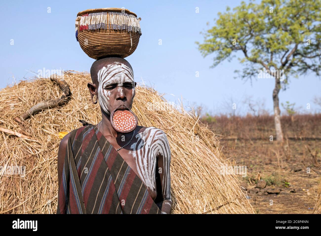 Donna dipinta della tribù Mursi con un piatto e un cesto in testa nel Parco Nazionale di Mago, Jinka, zona Debub Omo, Etiopia meridionale, Africa Foto Stock
