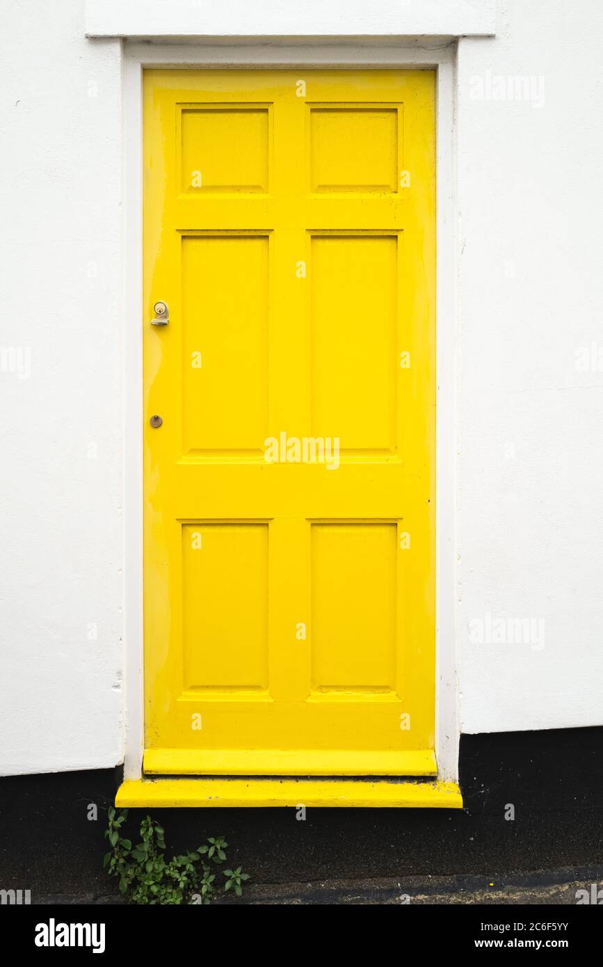 Semplice design di legno giallo porta d'ingresso ad una casa residenziale la parete circostante è bianca con una base nera. Foto Stock