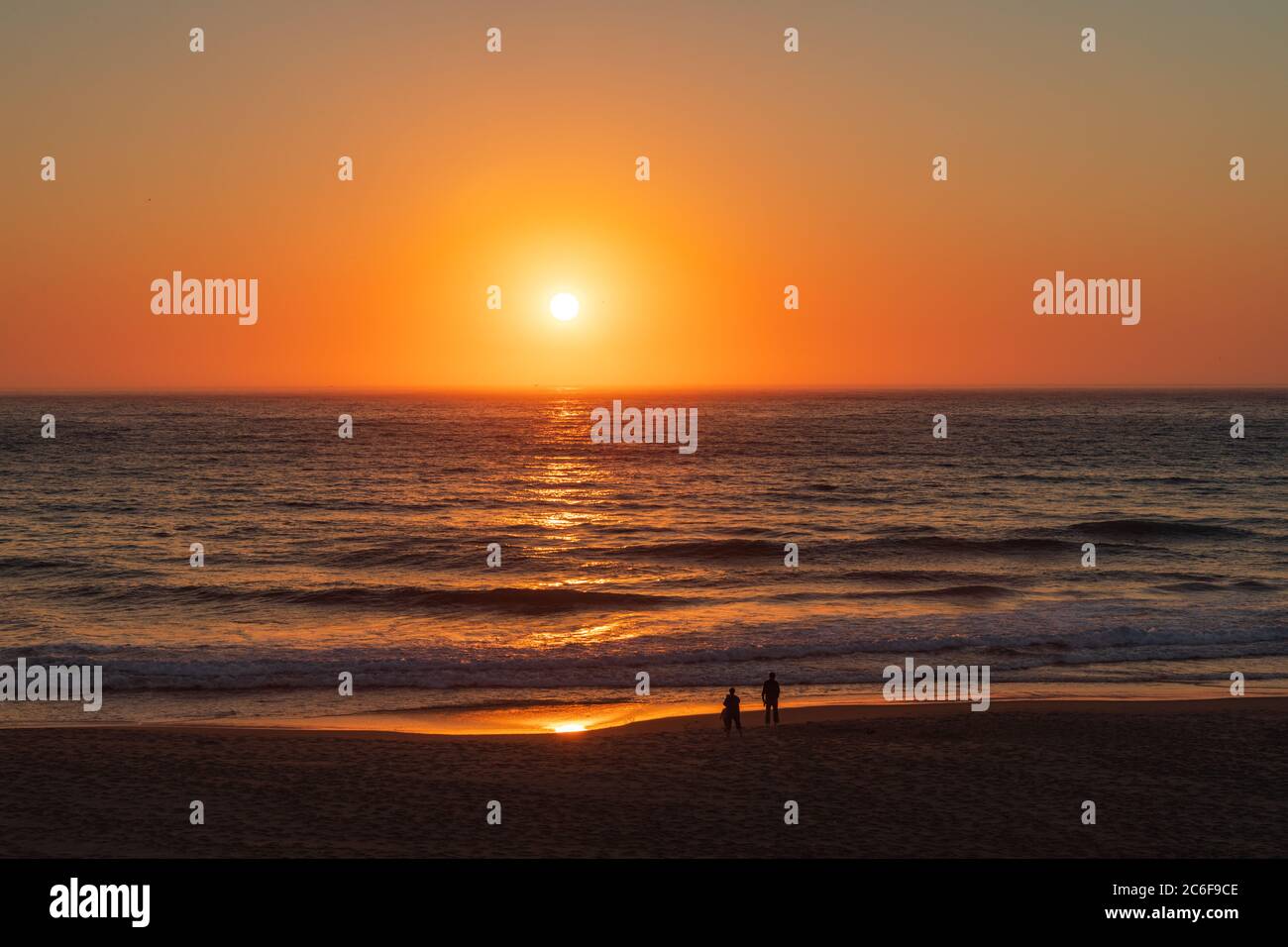 Un sole arancione crea un'incandescenza dorata nel cielo e dall'altra parte dell'acqua fino a una spiaggia sabbiosa dell'Oregon. Foto Stock