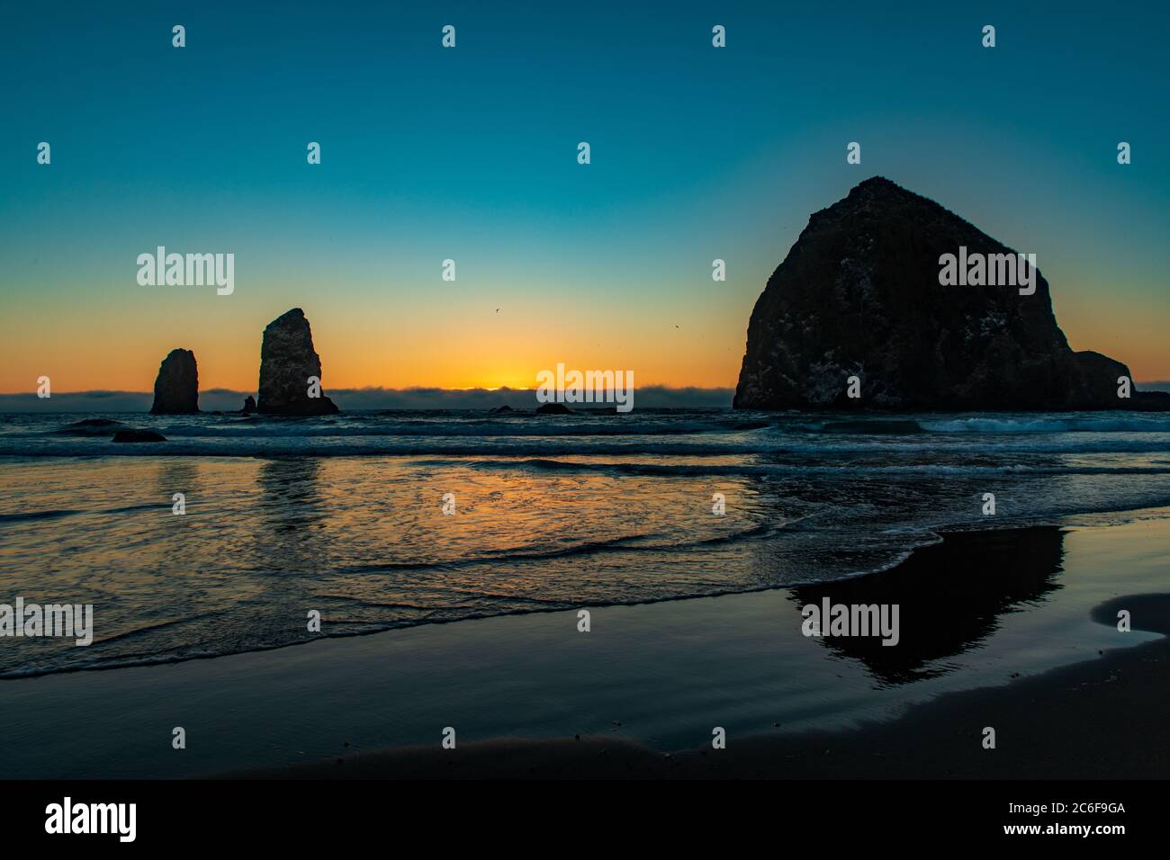 Il tramonto arancione mostra la silhouette di Haystack Rock e uccelli su Cannon Beach in Oregon Foto Stock