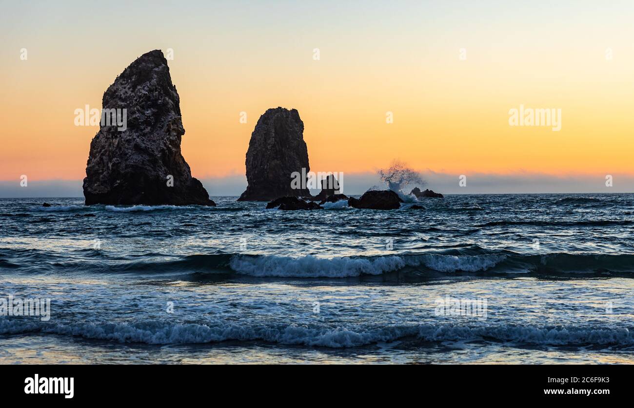 Il tramonto arancione mostra la silhouette delle onde che spruzzano sulle Sea Stack di Cannon Beach in Oregon Foto Stock