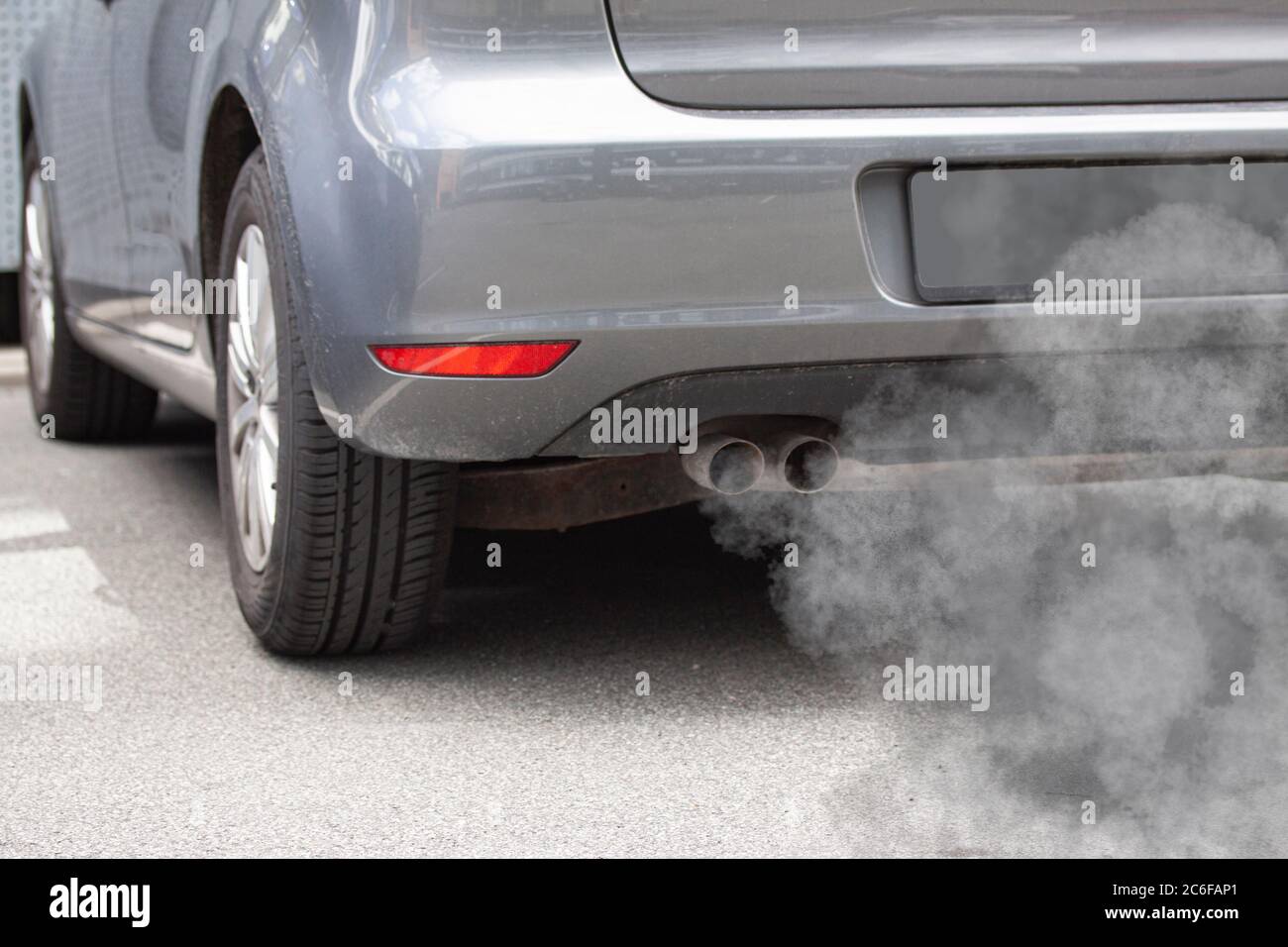 Tubo di scarico di un'automobile che soffia fuori l'inquinamento dalla parte posteriore di un'automobile grigia. Foto Stock