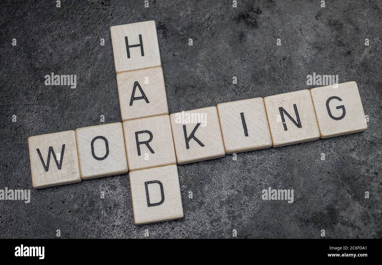 piastrelle di legno per lettere che formano parole su una superficie di ghisa grigia sullo sfondo, lavorando sodo Foto Stock