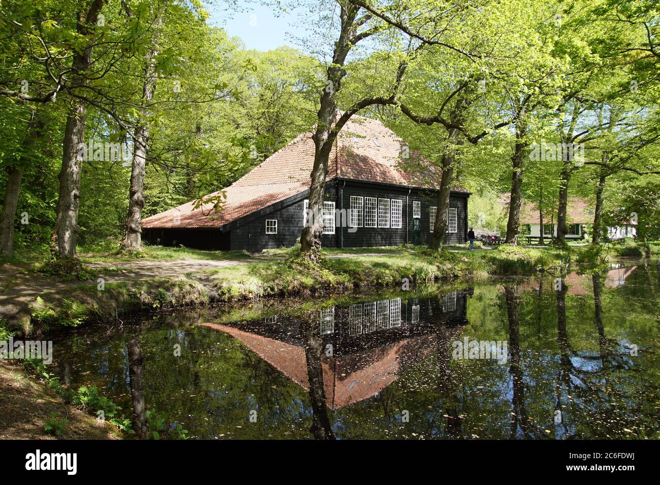 Una vecchia casa nera con tegole rosse nella foresta vicino all'acqua vicino al villaggio olandese di Bergen in primavera. Foto Stock