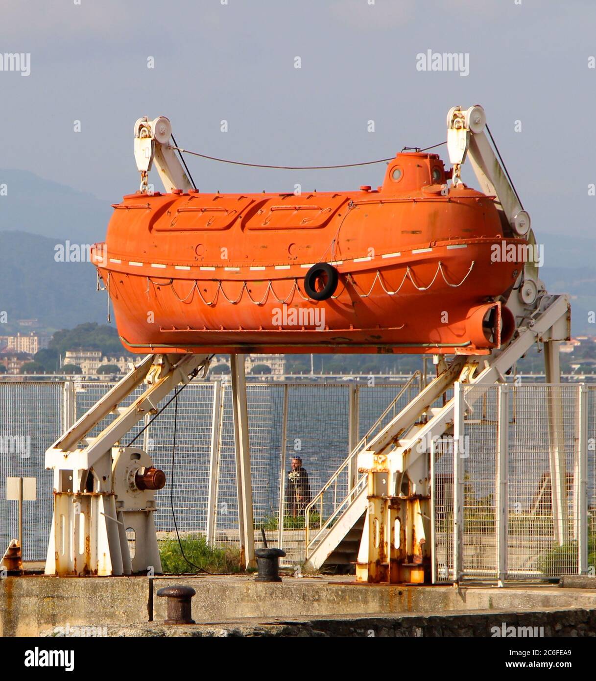 Arancione luminoso decommissionato capsula vita barca sospeso in una cornice di lancio bianco vicino alla baia di Santander Cantabria Spagna Foto Stock