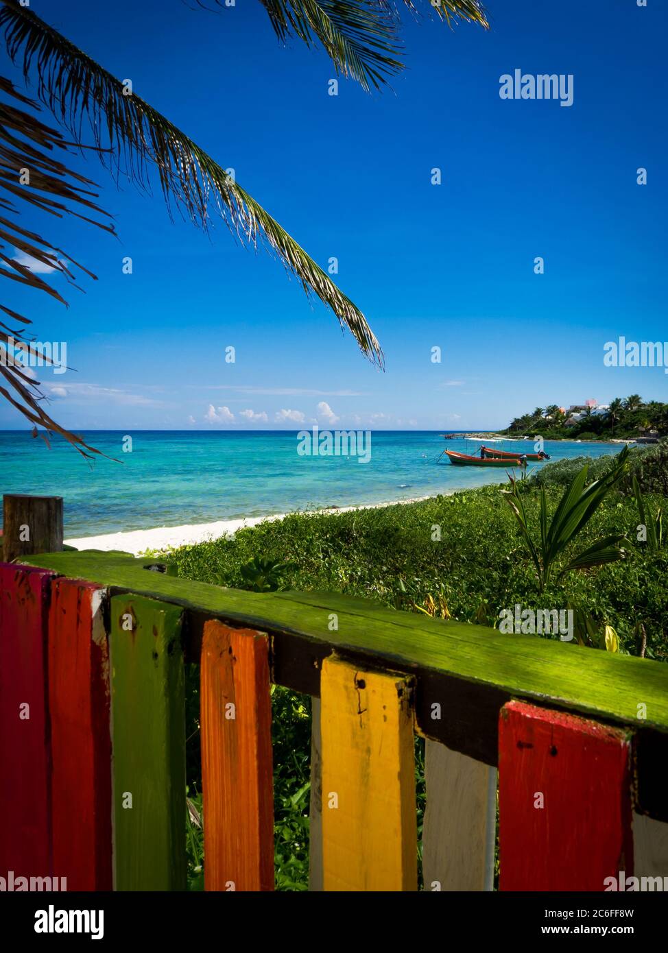 baia caraibica con barche fisher sullo sfondo e una colorata recinzione in legno in primo piano, immagine verticale Foto Stock