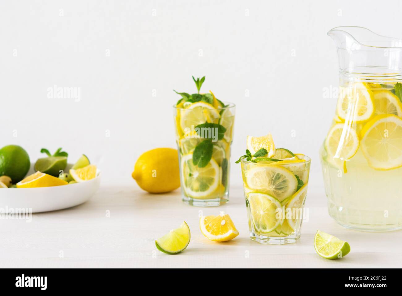 Bevanda estiva rinfrescante di limone, lime e menta, caraffa con limonata e bicchieri e fette di agrumi Foto Stock