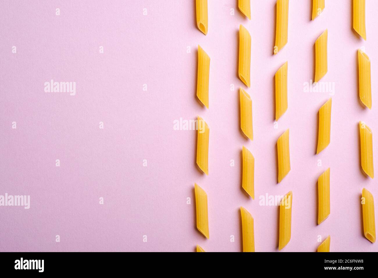 Pasta italiana, tubo crudo di penne macaroni su sfondo rosa, vista dall'alto spazio copia, cibo astratto Foto Stock