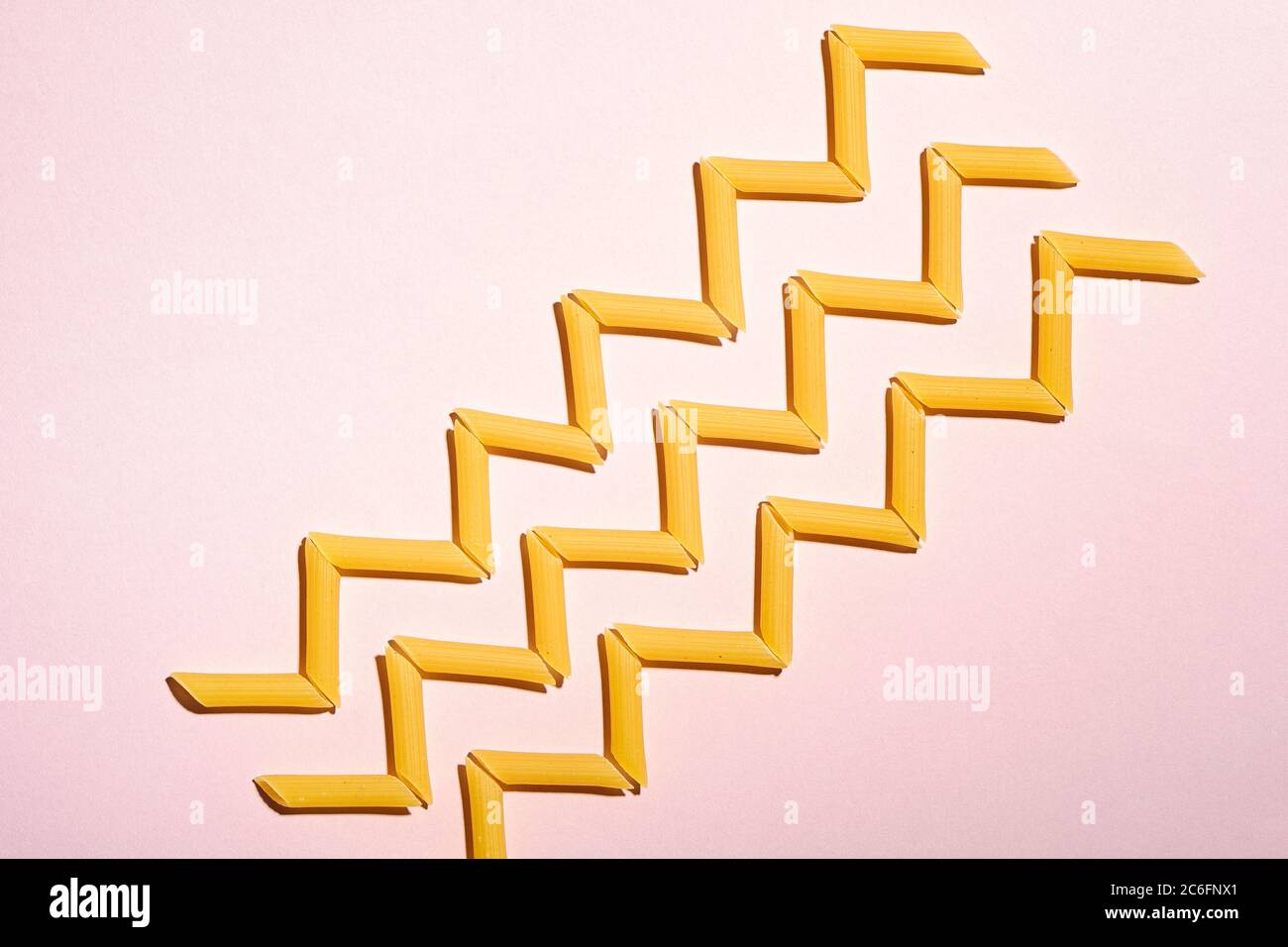 Pasta italiana, tubo crudo penne macaroni zigzag motivo su sfondo rosa, vista dall'alto copy space, cibo astratto Foto Stock