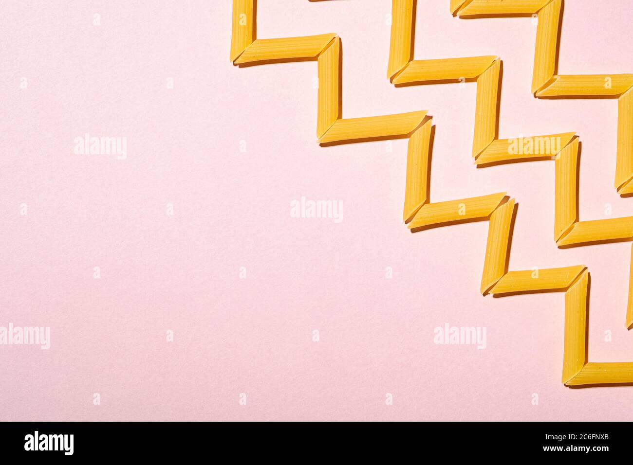Pasta italiana, tubo crudo penne macaroni zigzag motivo su sfondo rosa, vista dall'alto copy space, cibo astratto Foto Stock