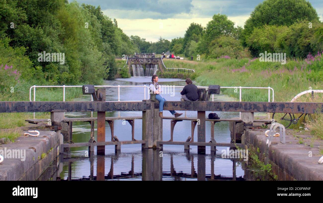 Glasgow, Scozia, Regno Unito 9 luglio 2020: Regno Unito Meteo: Sunny on the Forth e clyde Canal hanno visto la gente continuare a usarlo per esercitarsi e socializzare durante la chiusura mentre gli uomini locali si siedono sulle porte di chiusura ironicamente. Credit: Gerard Ferry/Alamy Live News Foto Stock