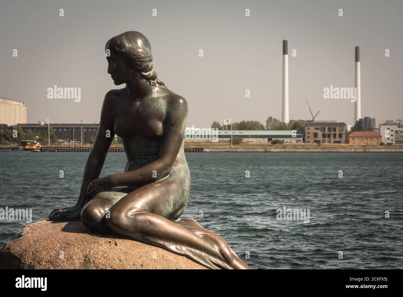 La statua della Sirenetta, situata di fronte ai due grandi camini di una centrale elettrica, Copenhagen, Danimarca Foto Stock