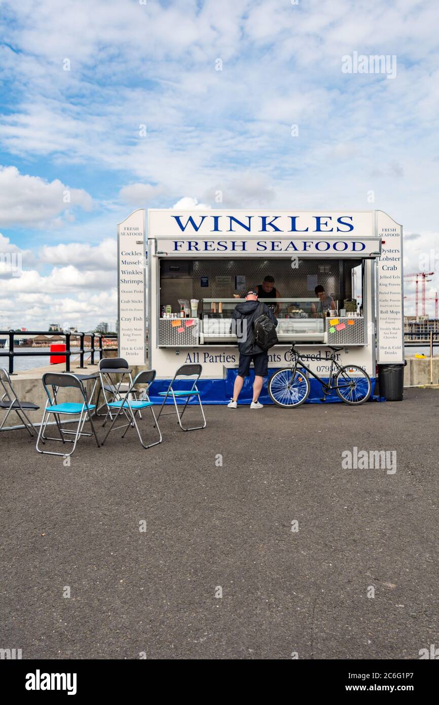 Un ciclista che aspetta di essere servito presso la tradizionale bancarella di pesce winkle affacciata sul Tamigi a Woolwich, sud-est di Londra, Inghilterra, Regno Unito Foto Stock