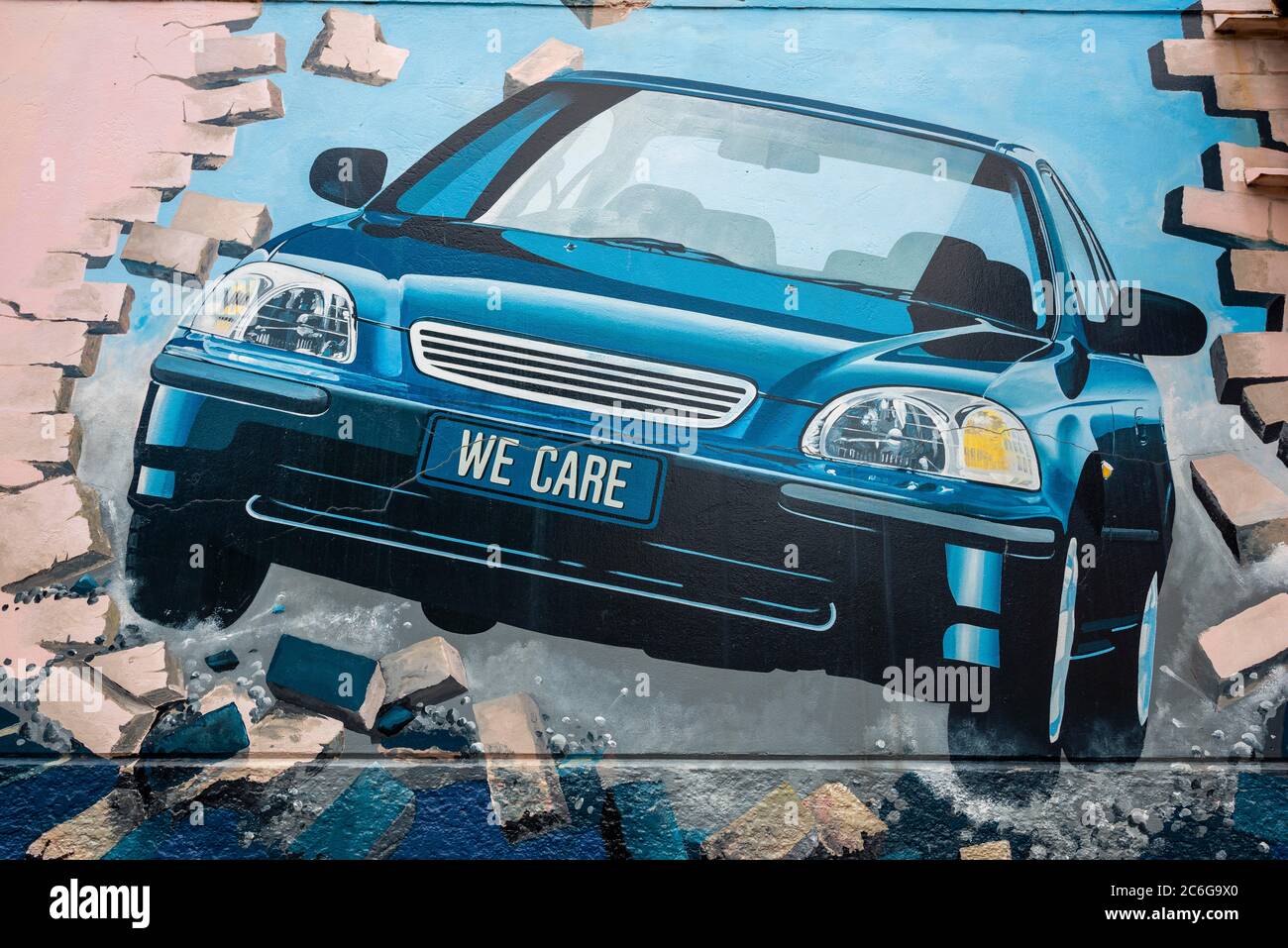 Graffiti, auto con iscrizione We Care guida attraverso muro, Dunedin, Otago, Nuova Zelanda Foto Stock