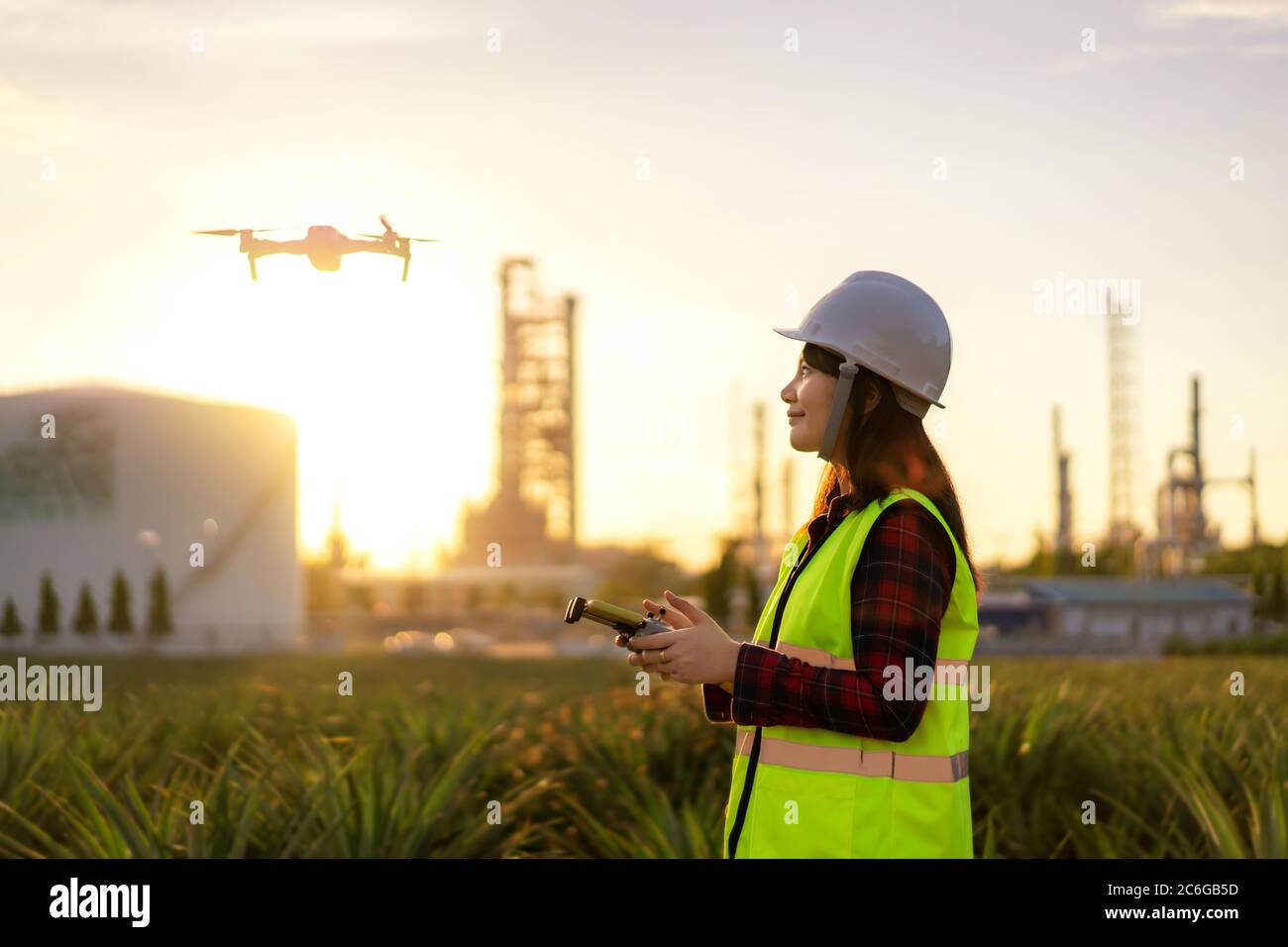 Ingegnere donna asiatico operare drone volo sopra l'impianto di raffineria di petrolio durante l'indagine sunrise cantiere in progetto di ingegneria civile. Foto Stock