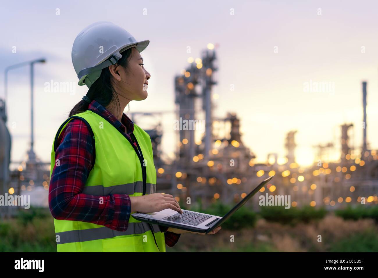 Donna asiatica ingegnere petrolchimico che lavora di notte con un computer portatile all'interno di petrolio e gas raffineria stabilimento di industria di notte per la sicurezza ispettore quali Foto Stock