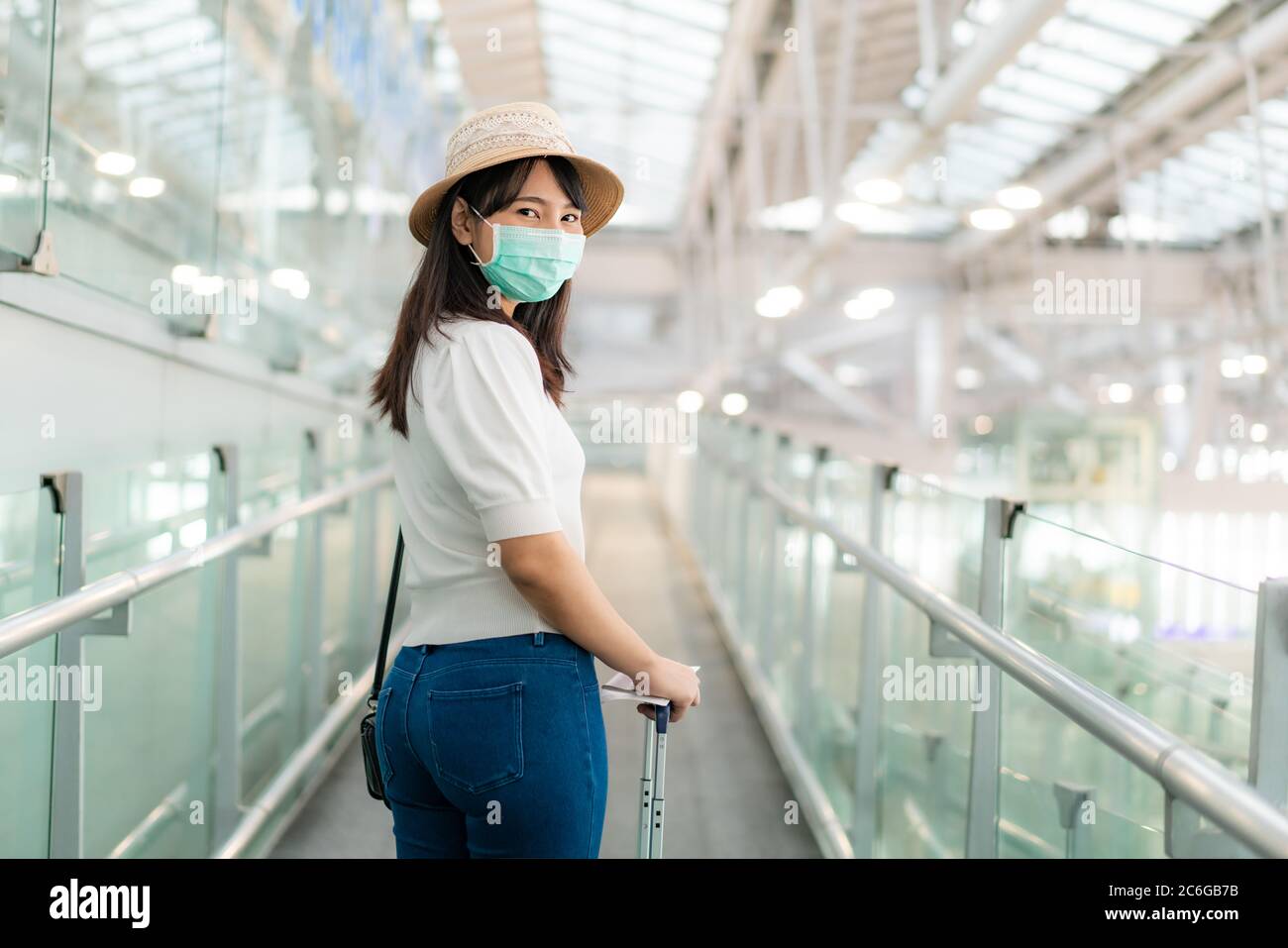 Donna asiatica viaggiatore che indossa maschera a piedi per salire a bordo del terminal dell'aeroporto e guardare la macchina fotografica e sorriso. Donna passeggero che viaggia in p Foto Stock