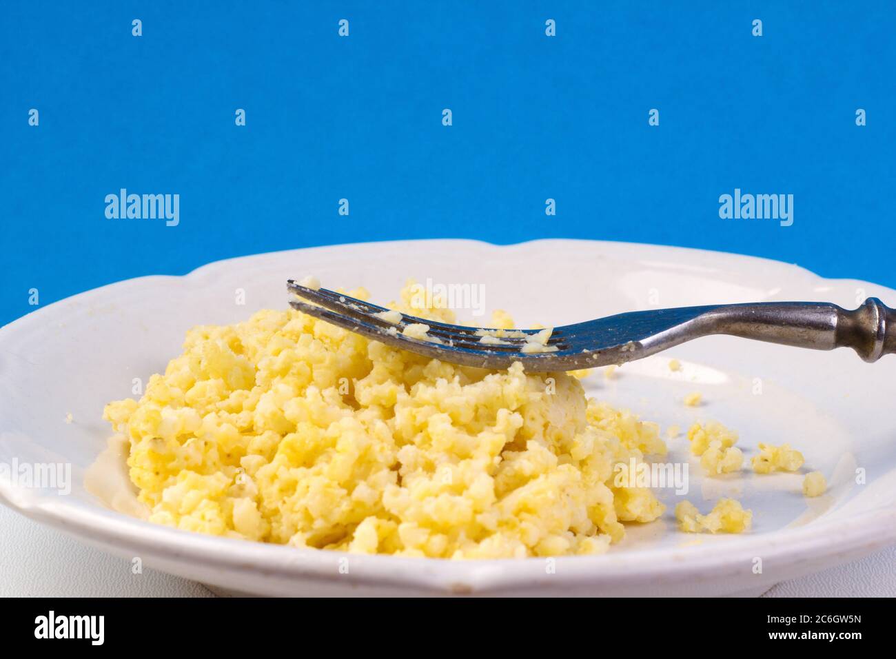 Porridge di miglio su un piatto bianco con forchetta su sfondo blu. Cibo vegetariano sano. Isolato su bianco Foto Stock