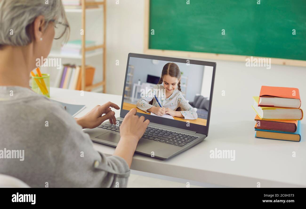L'insegnante in linea insegna un bambino. La bambina scrive una lezione in un notebook utilizzando una chat video con un insegnante di computer portatile a casa. Foto Stock