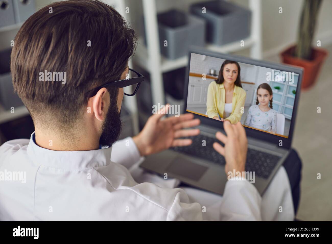 Il terapeuta medico maschile dà consigli per il trattamento di un bambino malato utilizzando un computer portatile video webcam mentre si siede in un ufficio di clinica. Foto Stock