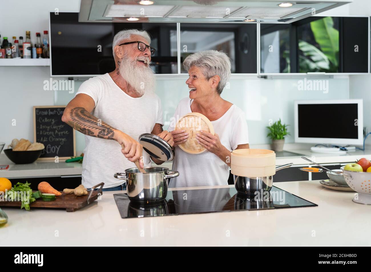 Felice coppia anziana che si diverte a cucinare insieme a casa - anziani che preparano un pranzo di salute in cucina moderna Foto Stock