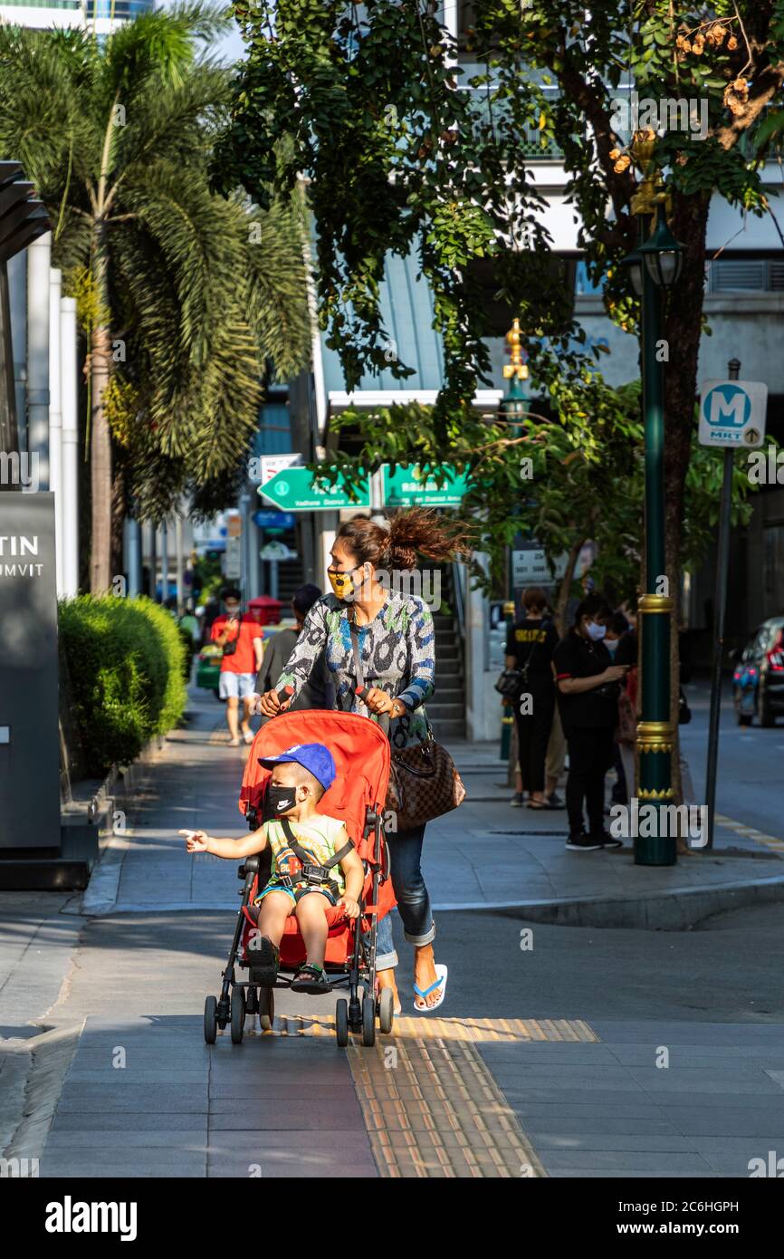 Ragazza che indossa maschera di spinta con la sedia di spinta con il bambino durante la pandemia di covid 19, Bangkok, Thailandia Foto Stock