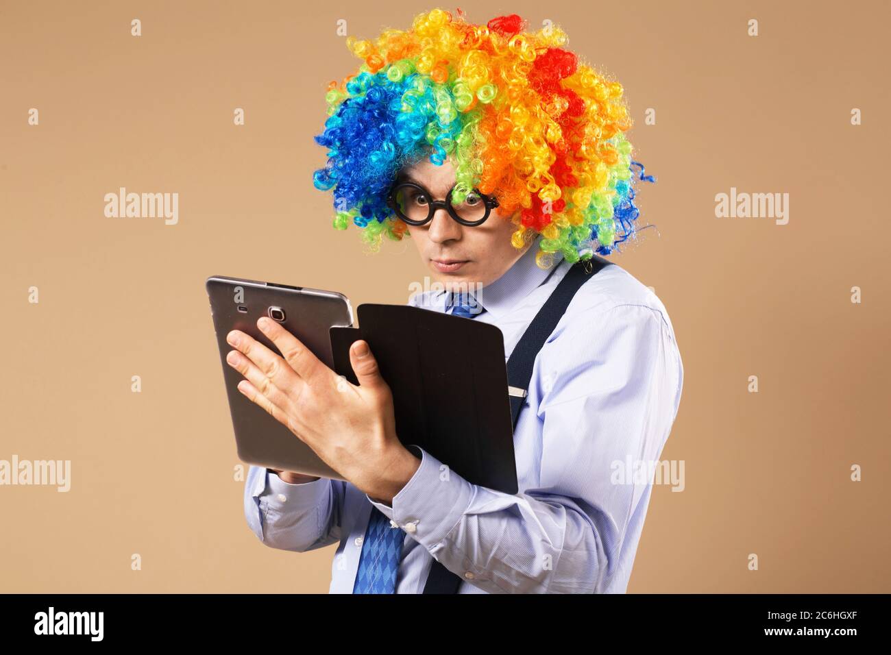 Uomo d'affari con computer tablet. Primo piano Ritratto di uomo d'affari in parrucca clown utilizzando un tablet per accedere a Internet. Concetto aziendale. Multitasking Foto Stock