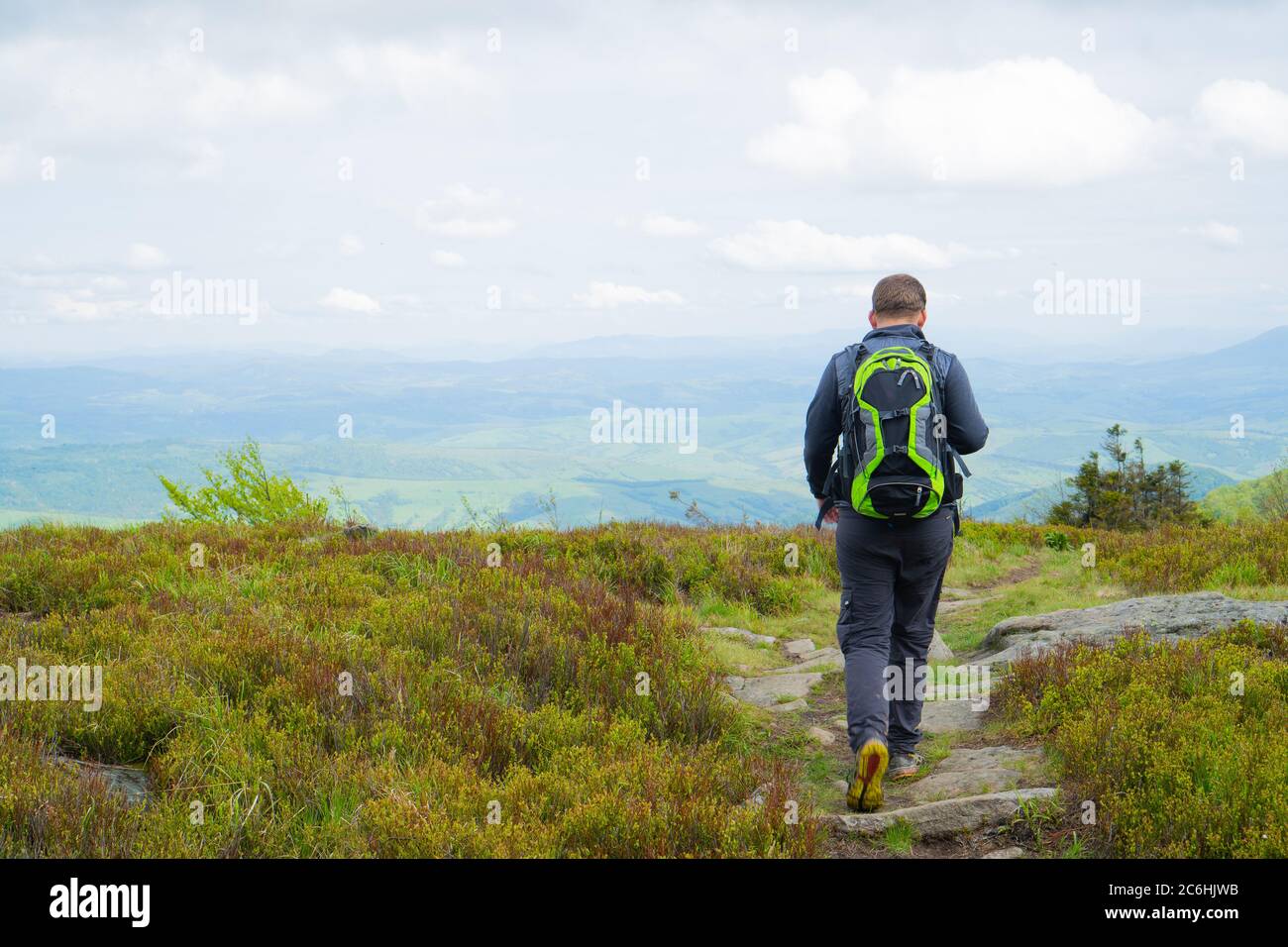 Uomo che parte dalla montagna per il sentiero roccioso. Il ragazzo in abiti da training grigio e uno zaino verde Foto Stock
