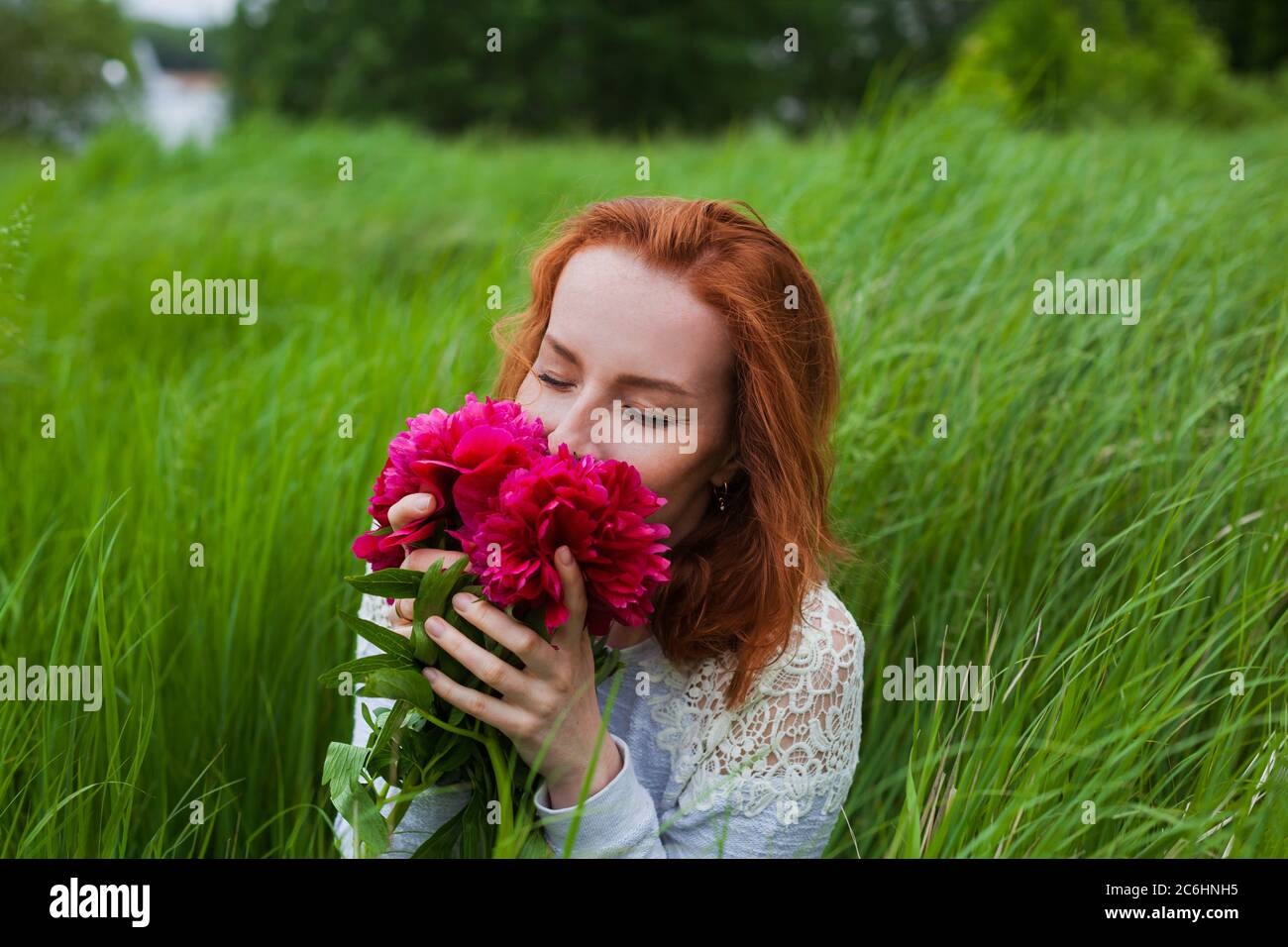La ragazza del Red head odori bouquet di peony nel campo Foto Stock