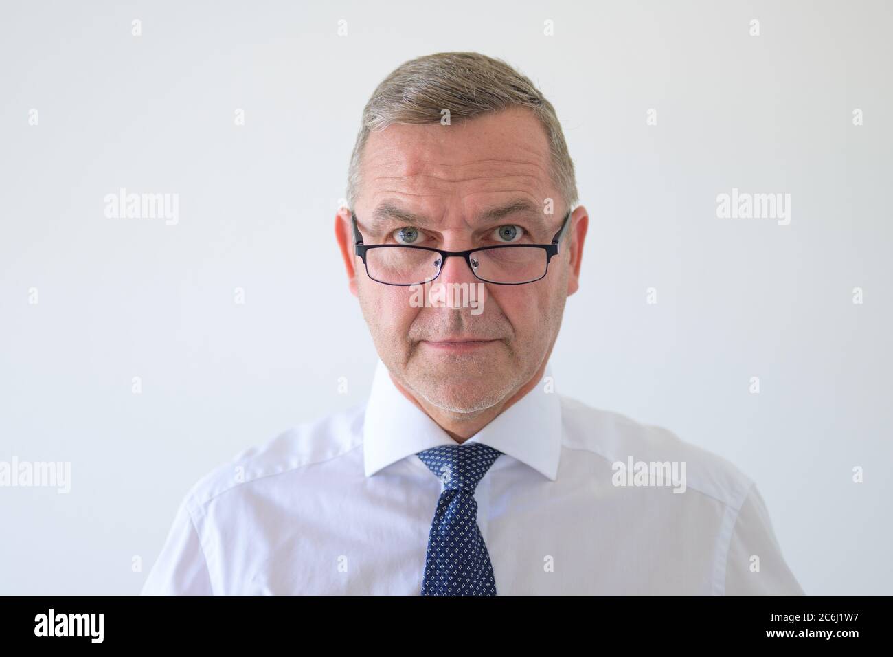 Uomo d'affari che guarda gli occhiali alla macchina fotografica con una seria espressione riflessiva in un ritratto di testa e spalle su bianco Foto Stock