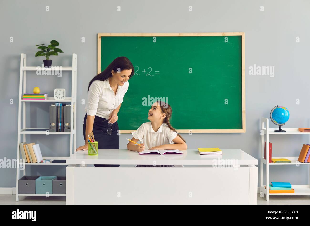 Insegnante insegna una studentessa in classe. Ritorno a scuola. Foto Stock
