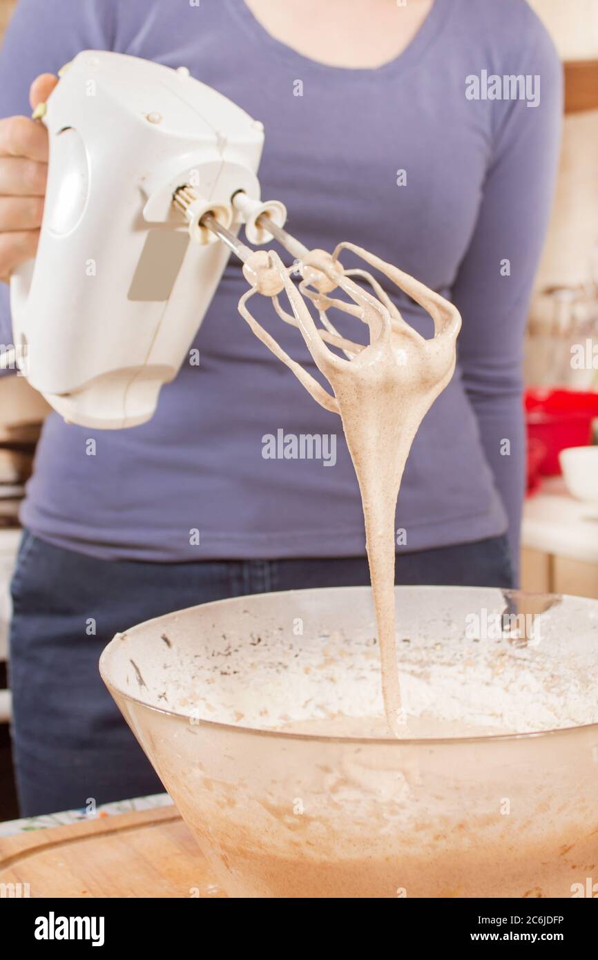 la donna sta tenendo un miscelatore. L'impasto scorre nel recipiente dalle lame del miscelatore. Preparare la cottura da una donna. Foto Stock