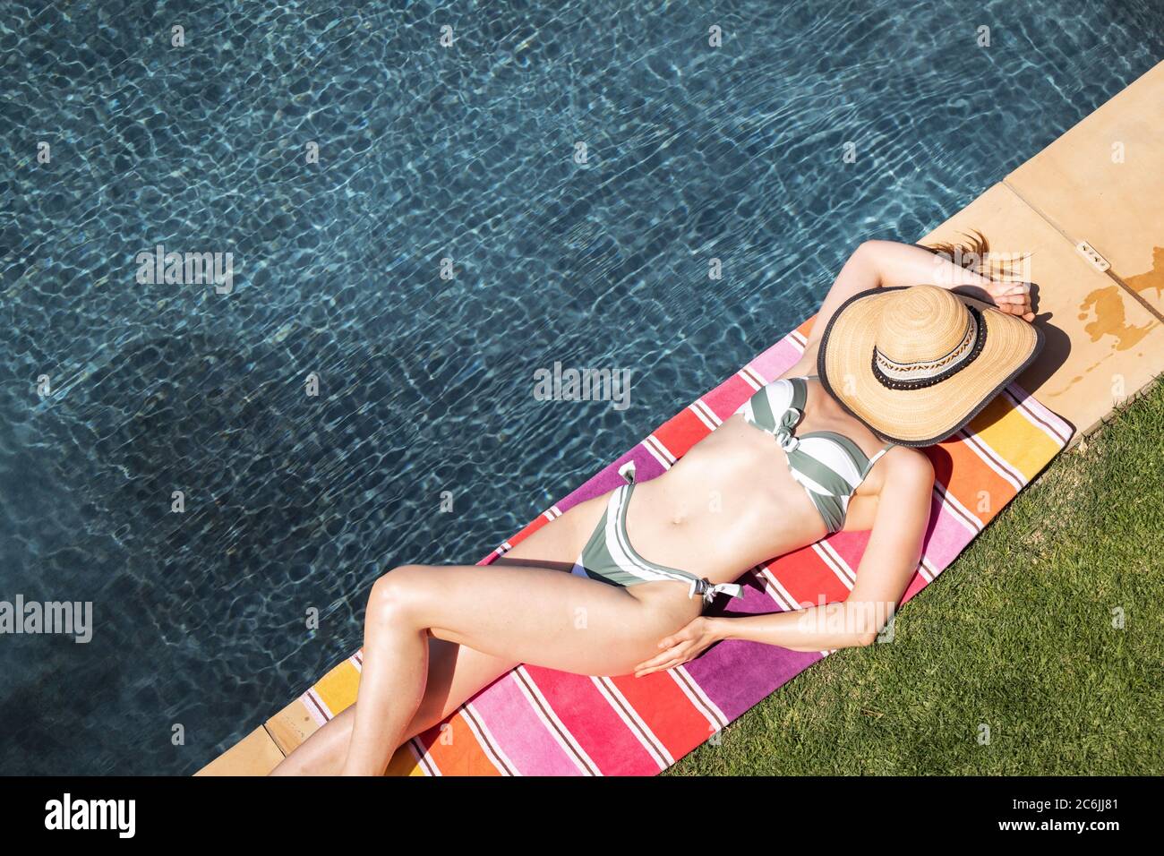 Donna con cappello sul viso che prende il sole in piscina Foto Stock