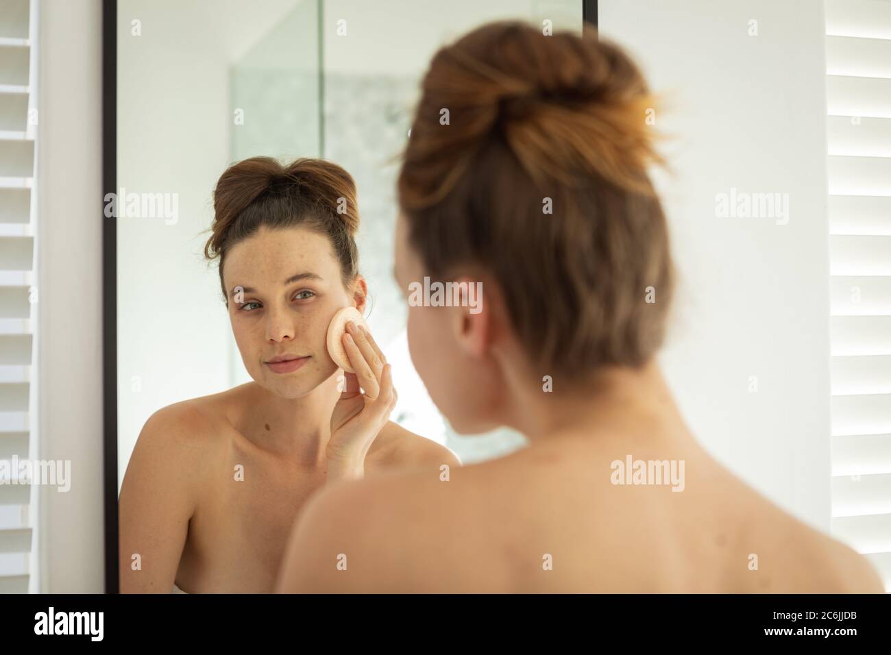 Donna che applica il trucco al suo viso mentre guarda nello specchio Foto Stock