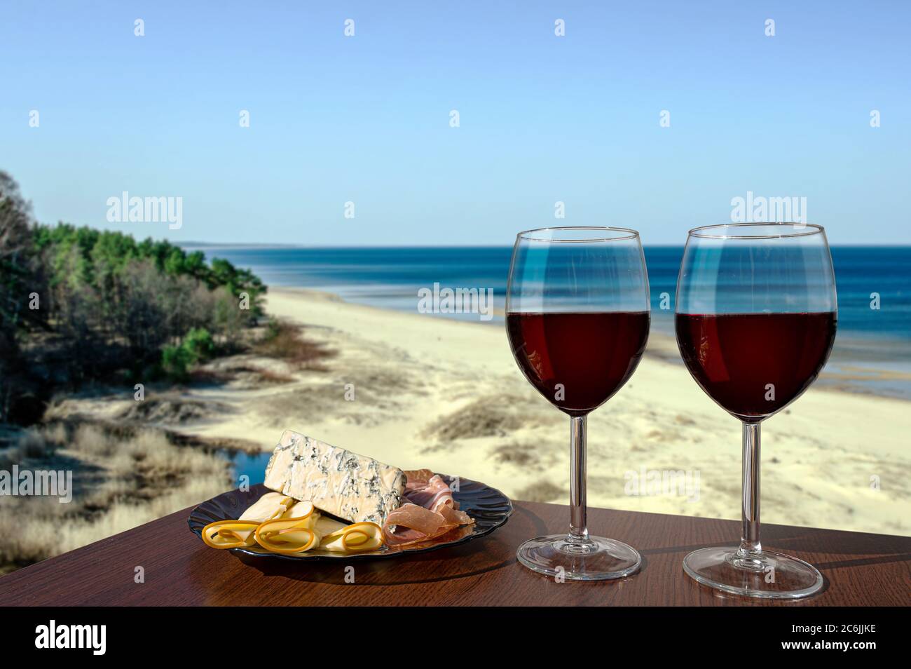 Due bicchieri di vino con assortimento di salumi con vista sulla spiaggia nel Mar Baltico. Bicchiere di vino rosso con diversi spuntini - piatto con prosciutto Foto Stock