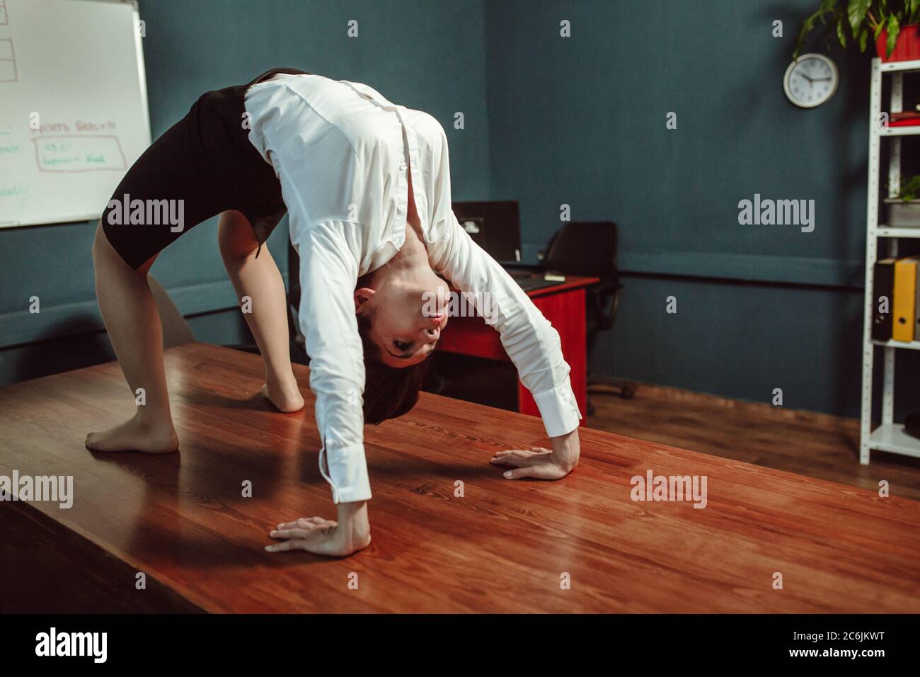 Fitness durante la pausa di lavoro. Giovane donna caucasica che fa esercizio in ponte alla scrivania dell'ufficio. Concetto di ricreazione. Concetto di yoga. Immagine colorata Foto Stock