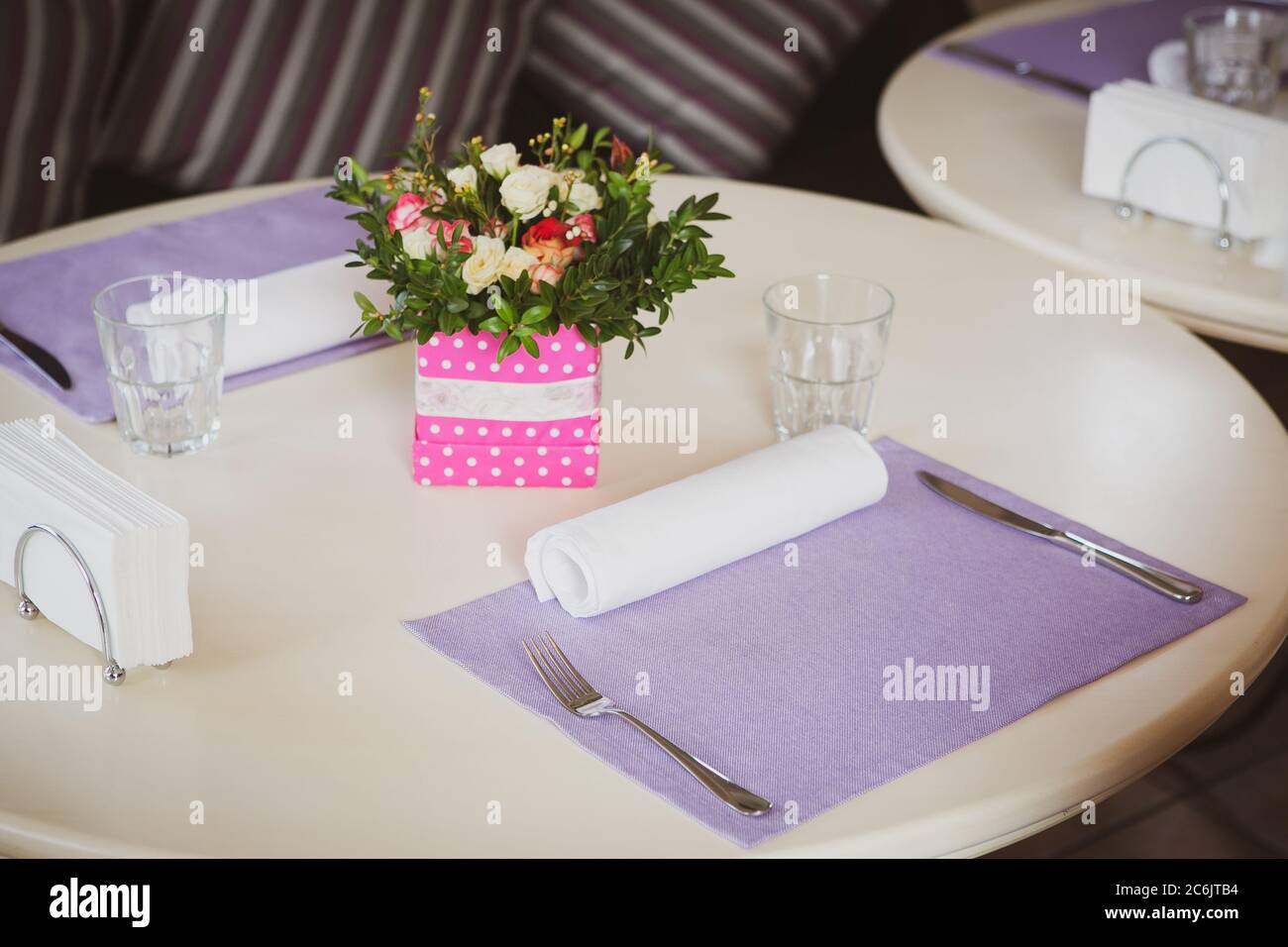 Romantico tavolo da pranzo con un grazioso decor floreale e tovaglioli viola in interni accoglienti. Concetto di anniversario o evento Foto Stock