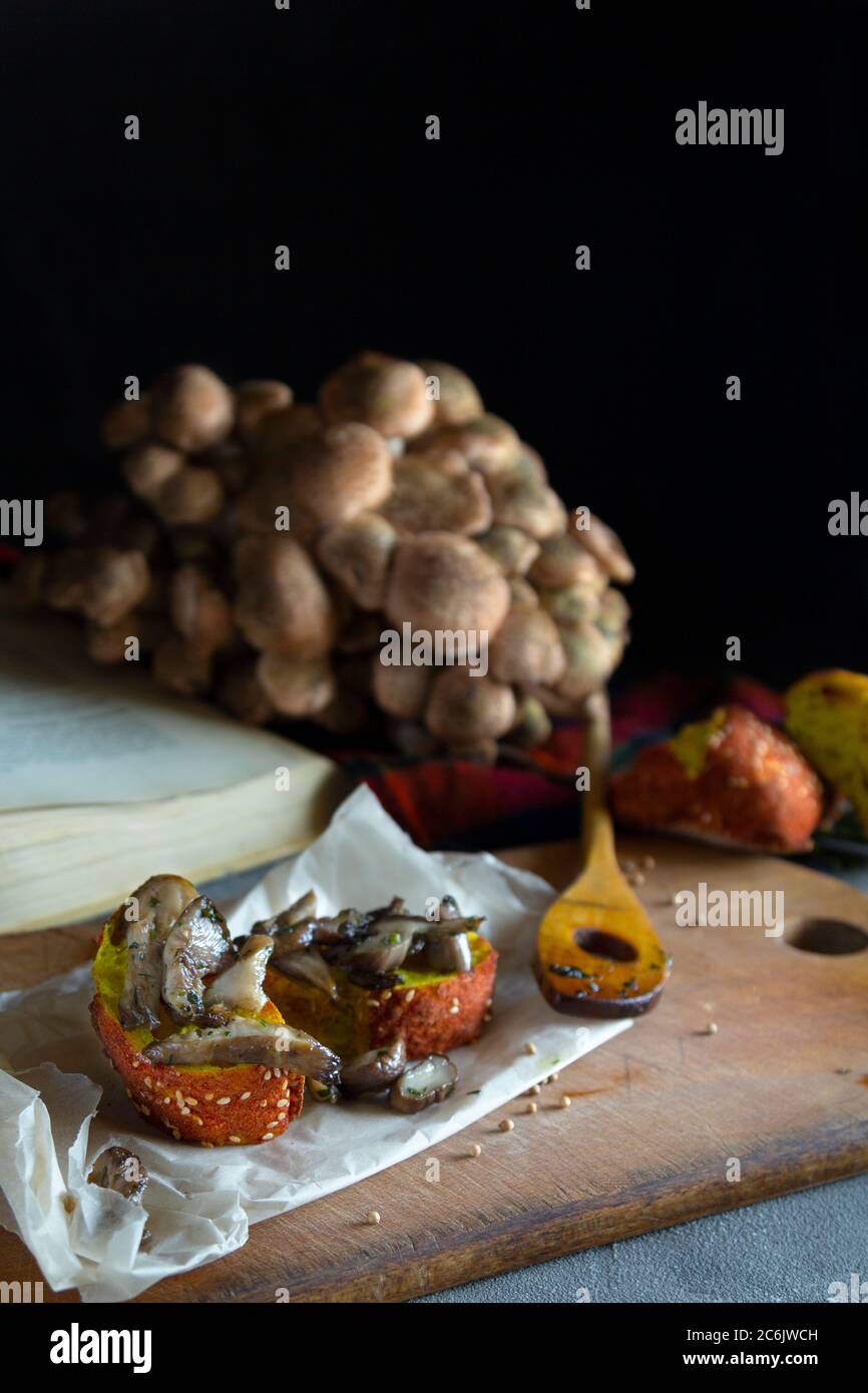 Funghi di bosco agarici di miele (Armillaria mellea). Composizione autunno ancora vita. Funghi fritti dorati su pane su tavola scura. Verticale Foto Stock