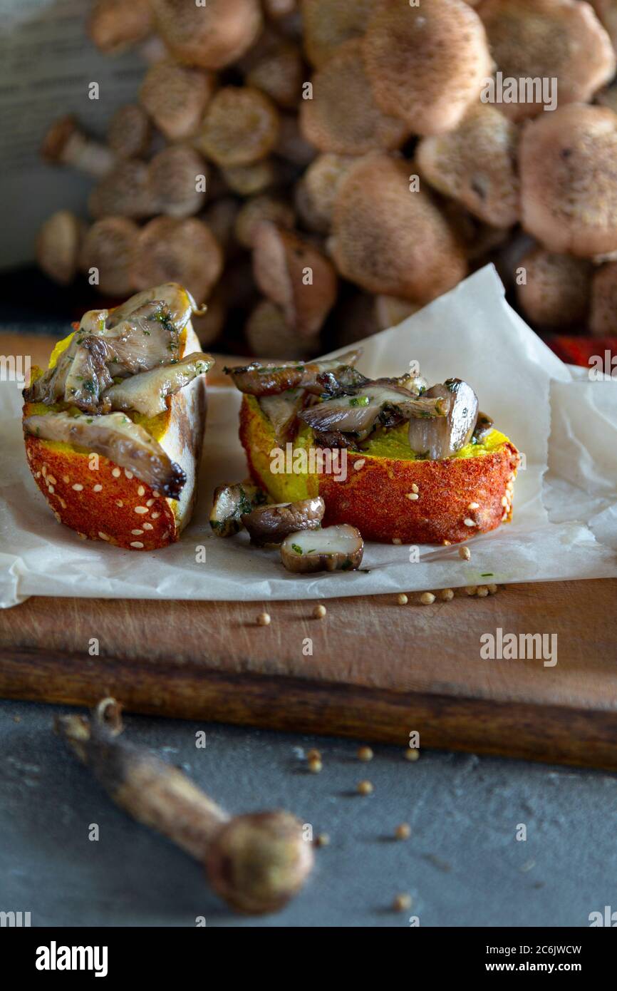 Funghi di bosco agarici di miele (Armillaria mellea). Composizione autunno ancora vita. Funghi fritti dorati su pane su tavola scura. Verticale Foto Stock