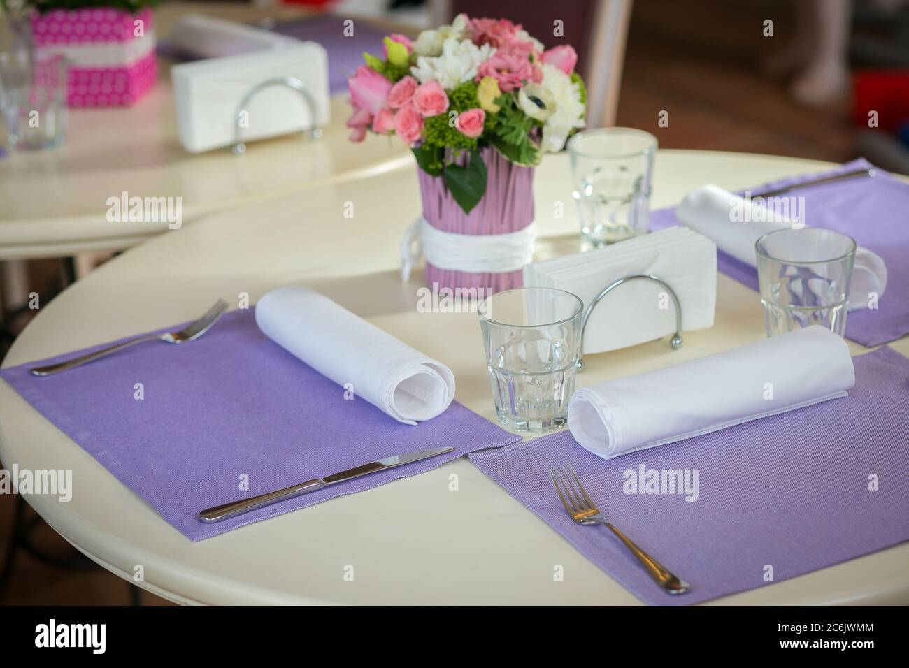 Decorazioni per celebrazioni chiare su un tavolo rotondo con bouquet di rose in un caffè aspetta i suoi ospiti. Concetto romantico. Concetto di evento o festa Foto Stock