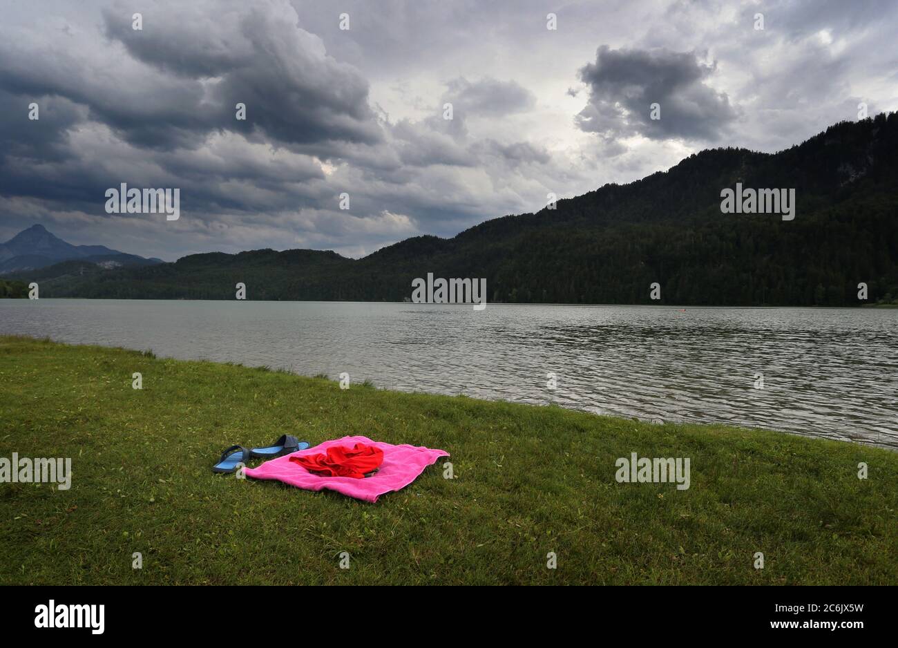 10 luglio 2020, Baviera, Füssen: Coperta e asciugamano - gli utensili di un bagnante si trovano sulla riva del lago Weissensee sotto le nuvole che si innalzano. Foto: Karl-Josef Hildenbrand/dpa Foto Stock