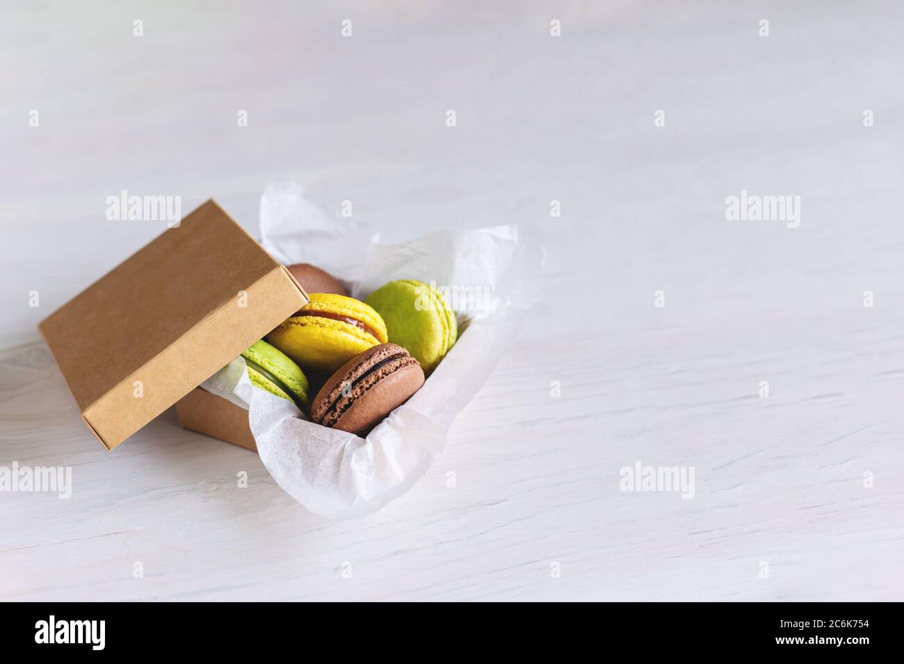 Gustosi macaron francesi in una scatola su un tavolo di legno bianco. Posiziona per il testo. Foto Stock