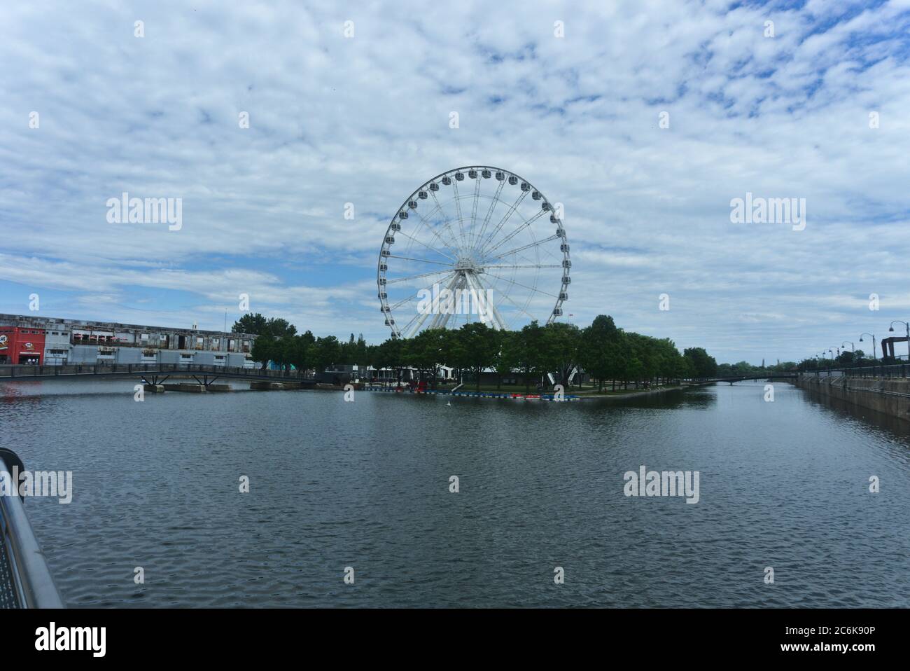 Ruota panoramica di Montreal nel porto vecchio. Lo sfondo è un cielo blu nuvoloso. In primo piano sono alberi e Saint Laurent fiume. Foto Stock