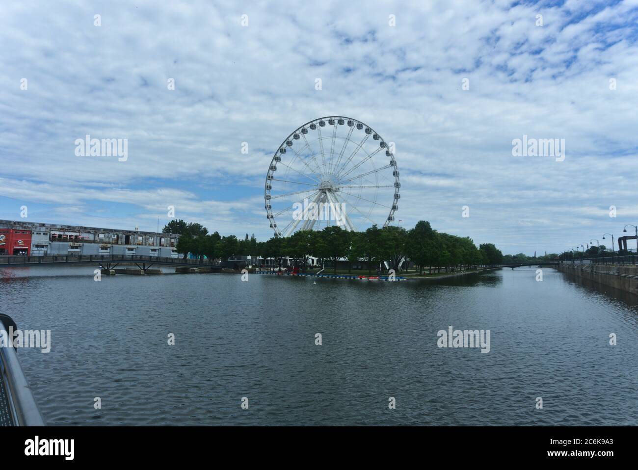 Ruota panoramica di Montreal nel porto vecchio. Lo sfondo è un cielo blu nuvoloso. In primo piano sono alberi e Saint Laurent fiume. Foto Stock