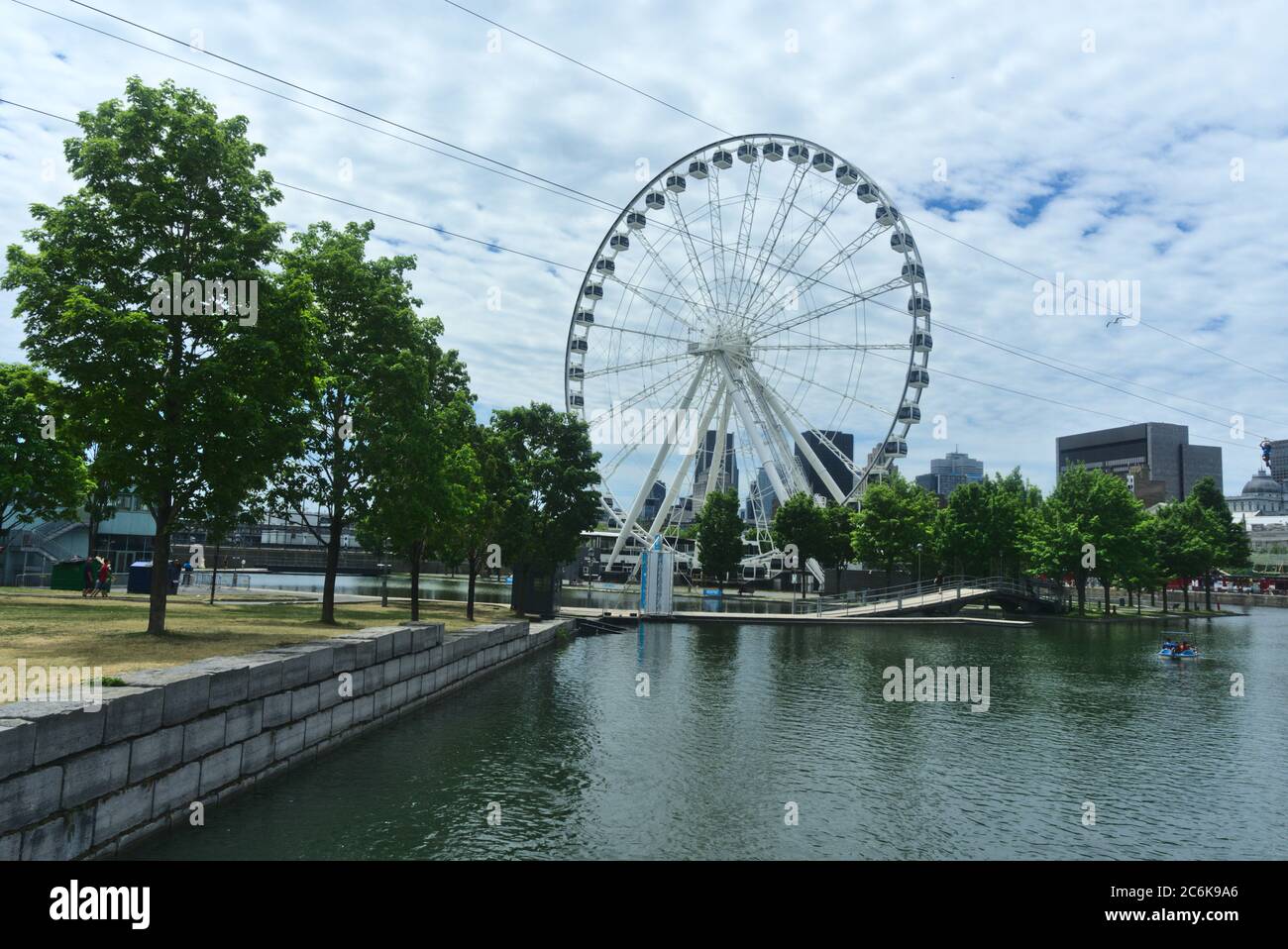 Ruota panoramica di Montreal nel porto vecchio. Lo sfondo è un cielo blu nuvoloso. In primo piano sono alberi e Saint Laurent fiume. Foto Stock