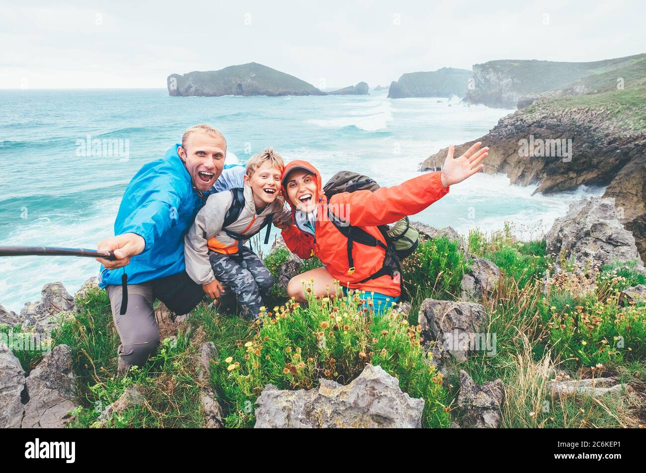 Felici viaggiatori due genitori famiglia con il loro figlio piccolo sulla costa del mare Cantabrico che si posano allegramente in macchina fotografica mentre vanno da Camino de Santiago Foto Stock