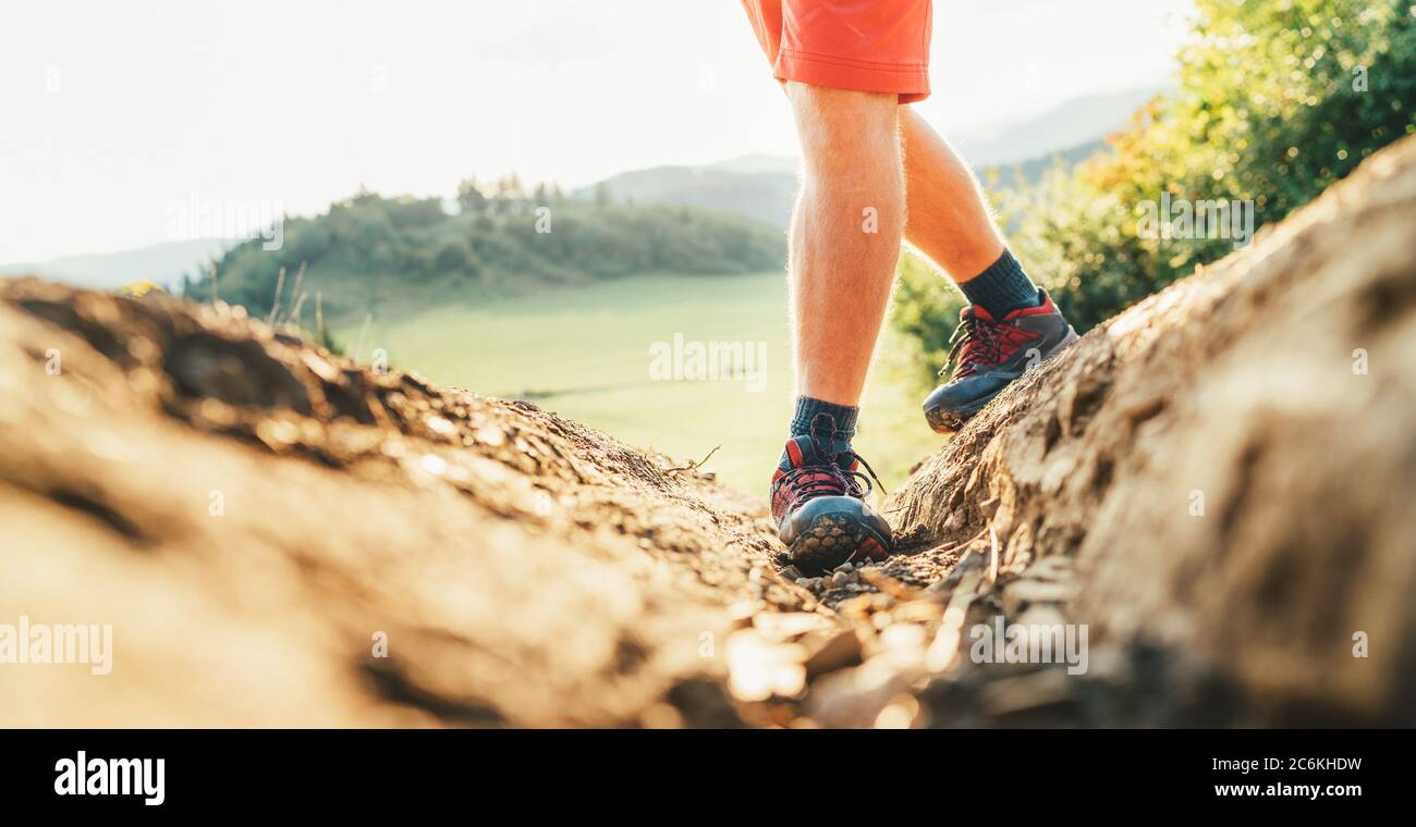 Primo piano immagine zaino in spalla piedi in scarpe da trekking su percorso di montagna sporco in estate giorno di sole. Foto Stock