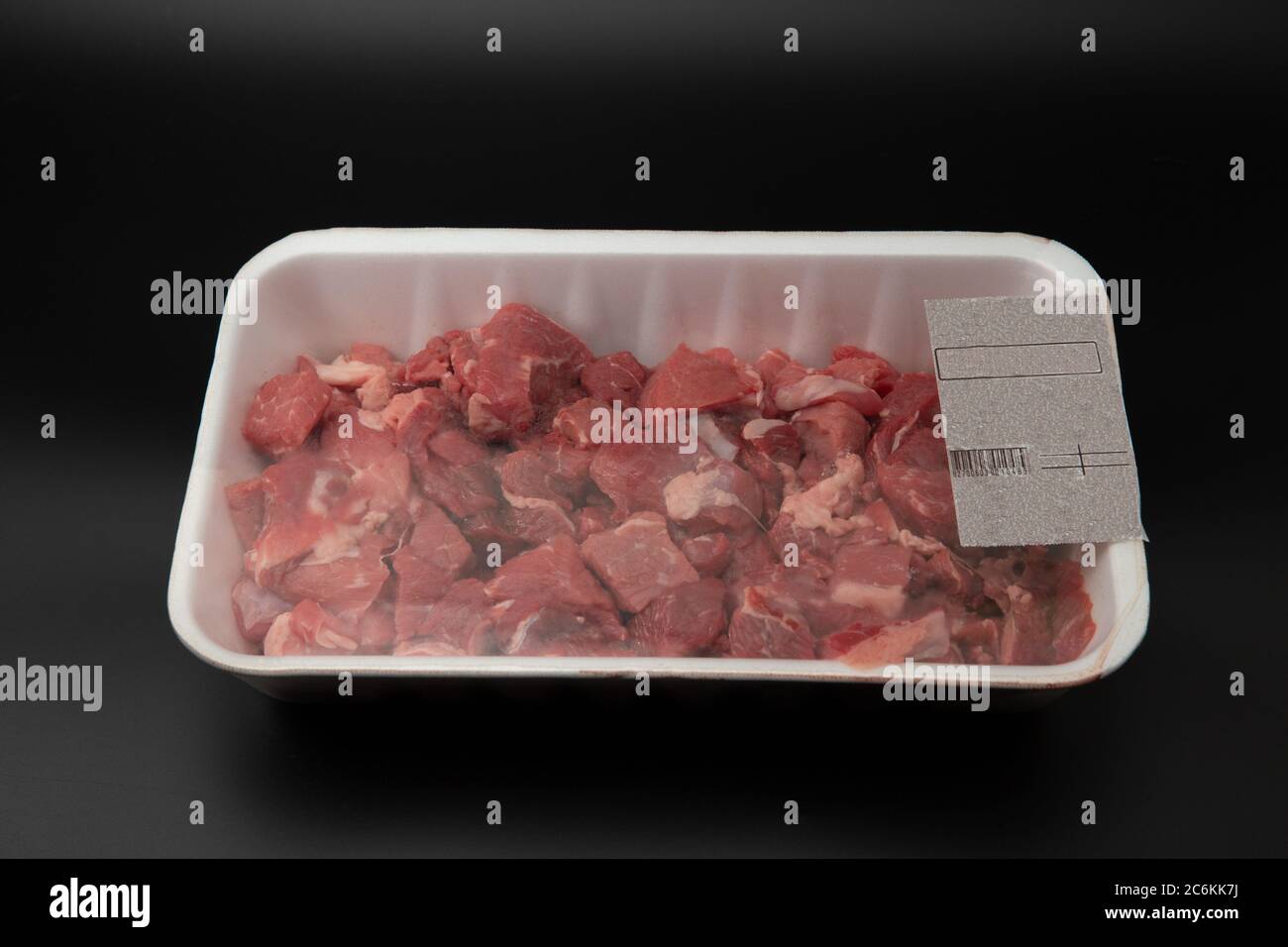 Carne grezza tagliata a cubetti in un contenitore bianco di polistirolo con codice a barre isolato su sfondo nero spazio per la copia del testo Foto Stock