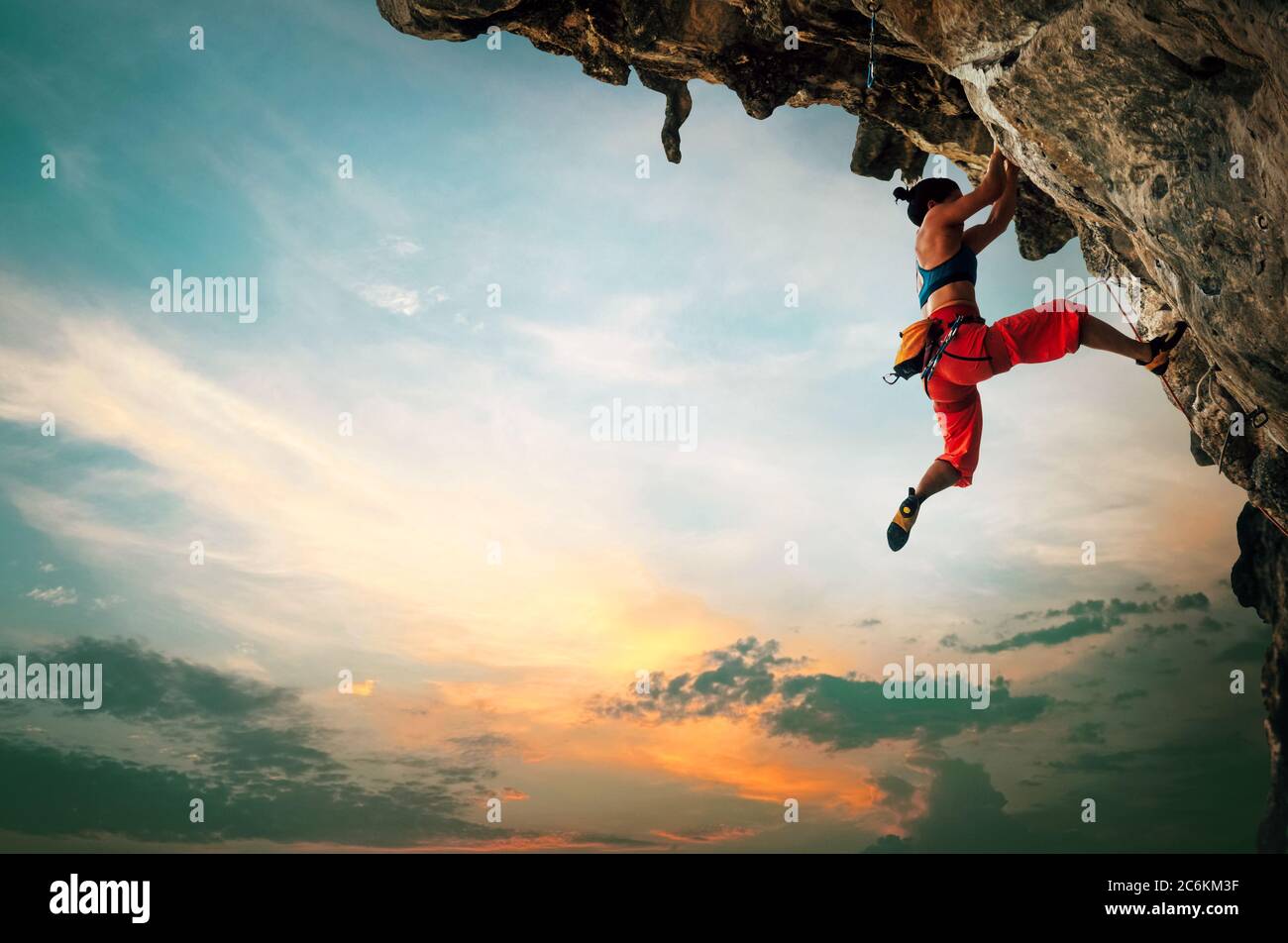 Donna atletica che sale su roccia a picco con sfondo cielo tramonto Foto Stock