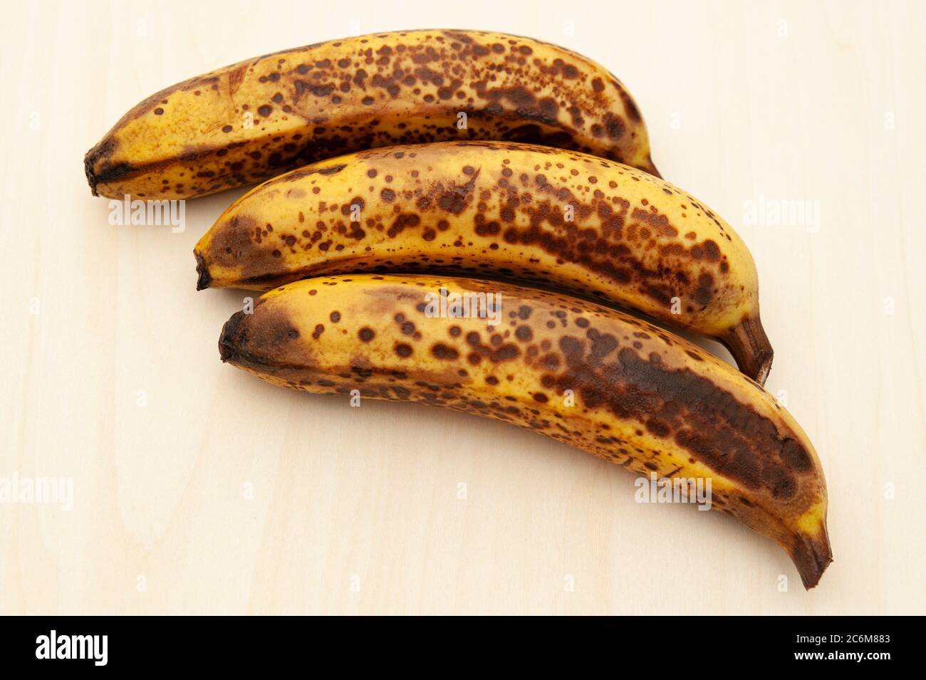 Tre banane mature isolate su sfondo di legno chiaro. Spazio di copia. Vista dall'alto. Foto Stock